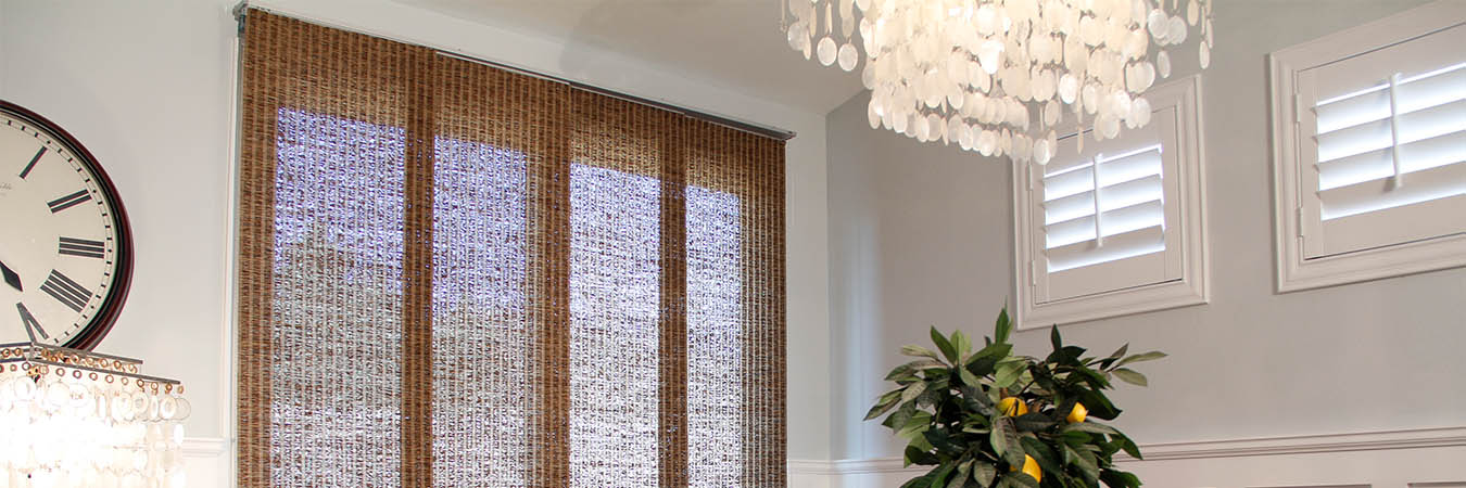 Woven fiber shades on a tall window and white Polywood shutters on small windows in a white dining room