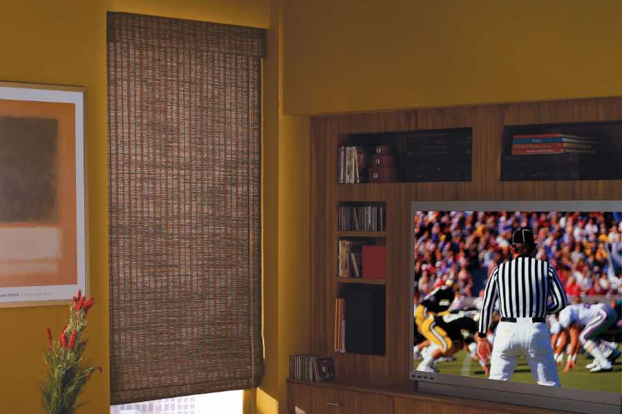 Use stylish woven shades to block unwanted light or give you privacy in your home. Brown woven shade on a TV room window