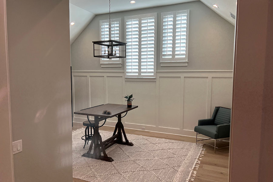 Attractive window treatments like Polywood shutters make your guest house more appealing to visitors. View through a doorway into a gray living space with white interior shutters on three windows
