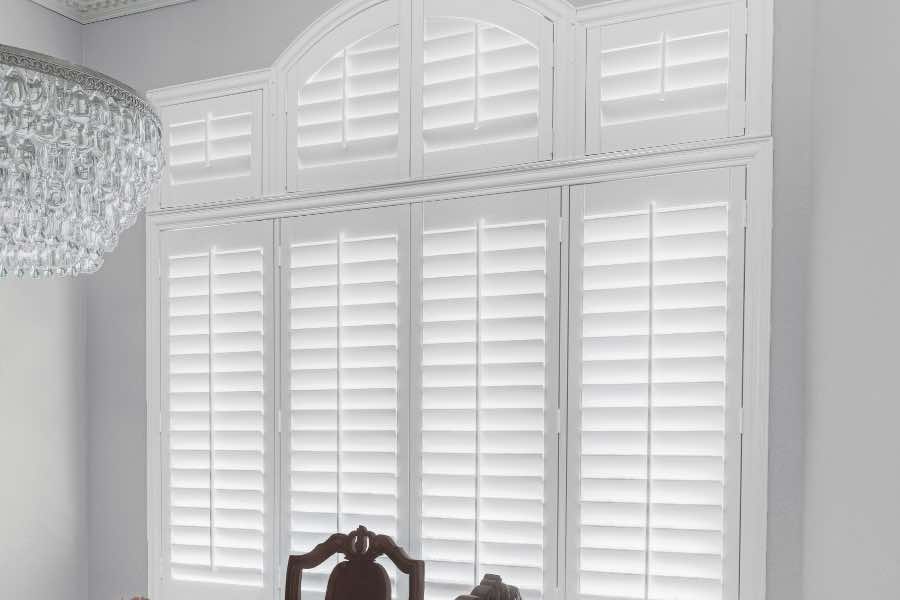 If you have an arched dining room window, Polywood shutters will cover your window without hiding its beautiful shape. Polywood shutters on a large window in a neutral-colored dining room